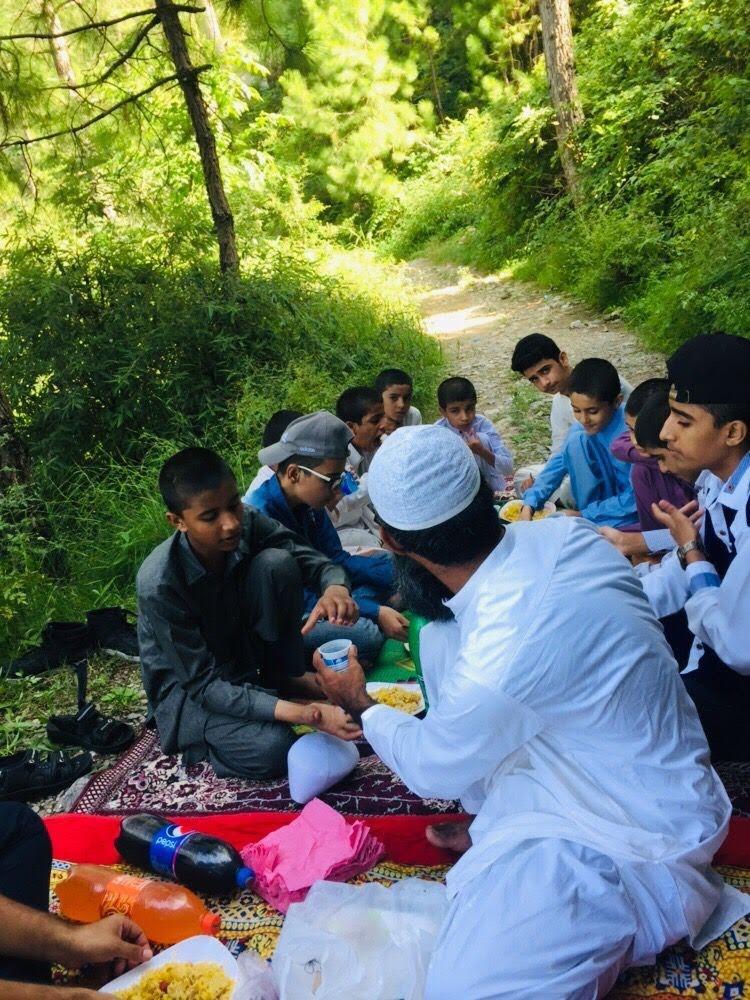 Children and a caregiver sharing a meal outdoors at Ashiana-e-Korang in Pakistan
